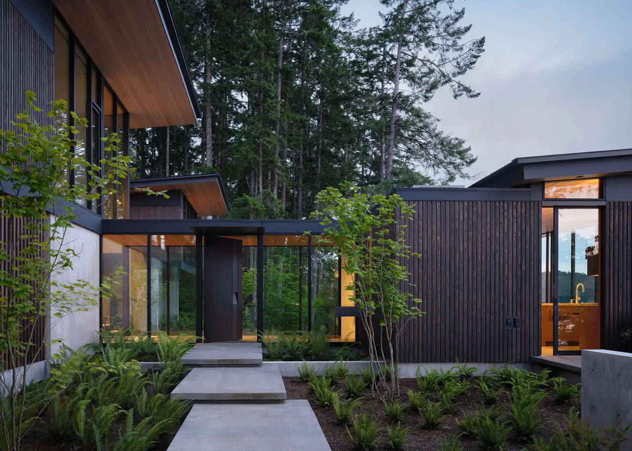 Modern residence with vertical wood siding and floor-to-ceiling glazing blends with forest surroundings.