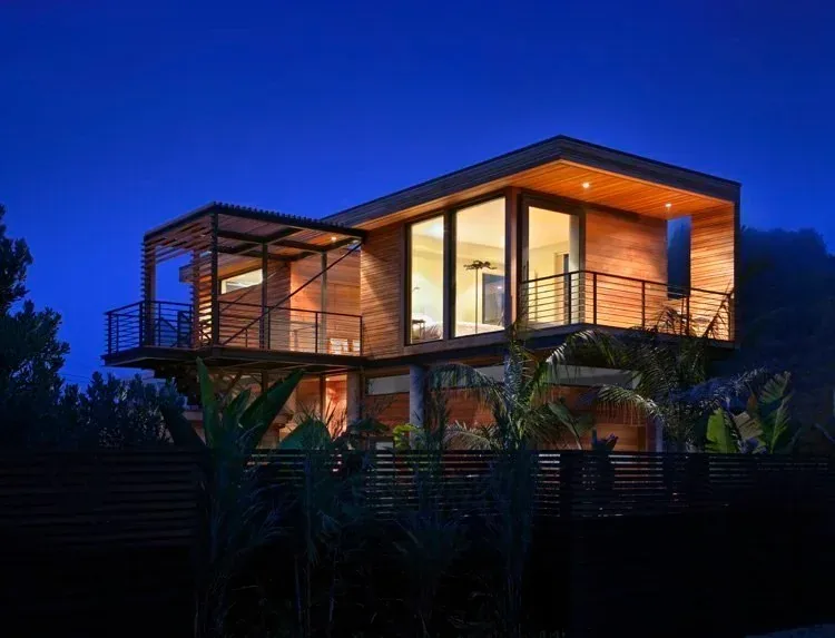 This floodproof house by Studio Peek Ancona features wood siding and large floor-to-ceiling windows, elevated above ground level.