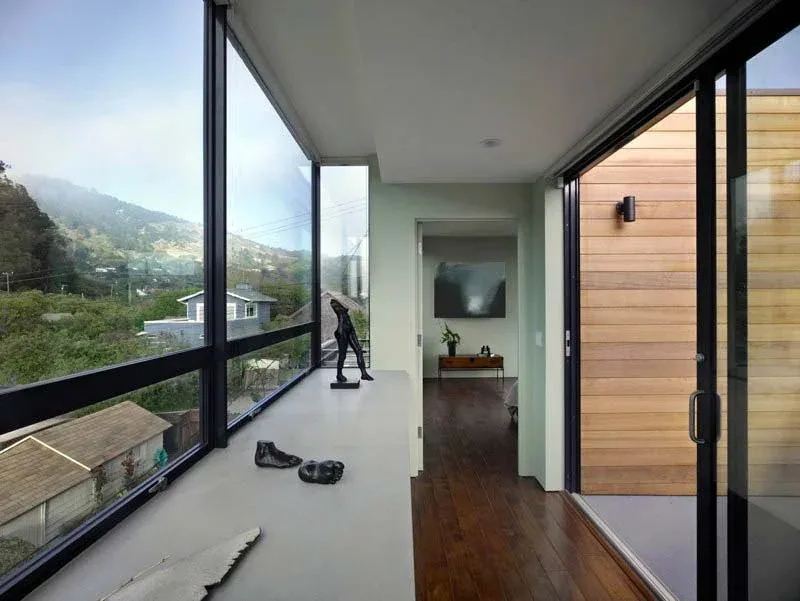 Hallway with floor-to-ceiling black window frames and sliding glass door opening to an exterior wood-clad wall.