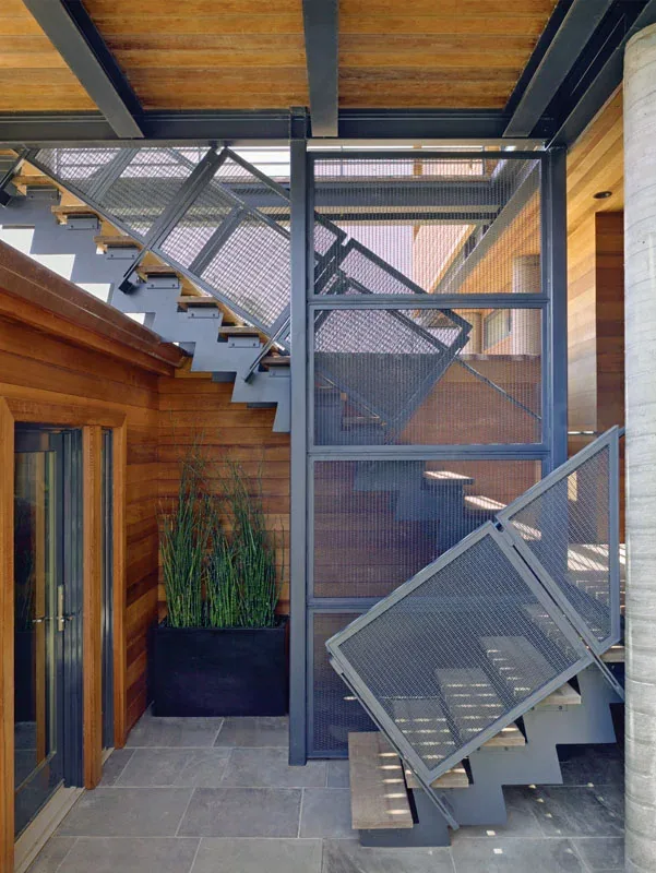 Interior view of a modern steel staircase with wood treads and perforated metal railings at Floodproofhouse project.