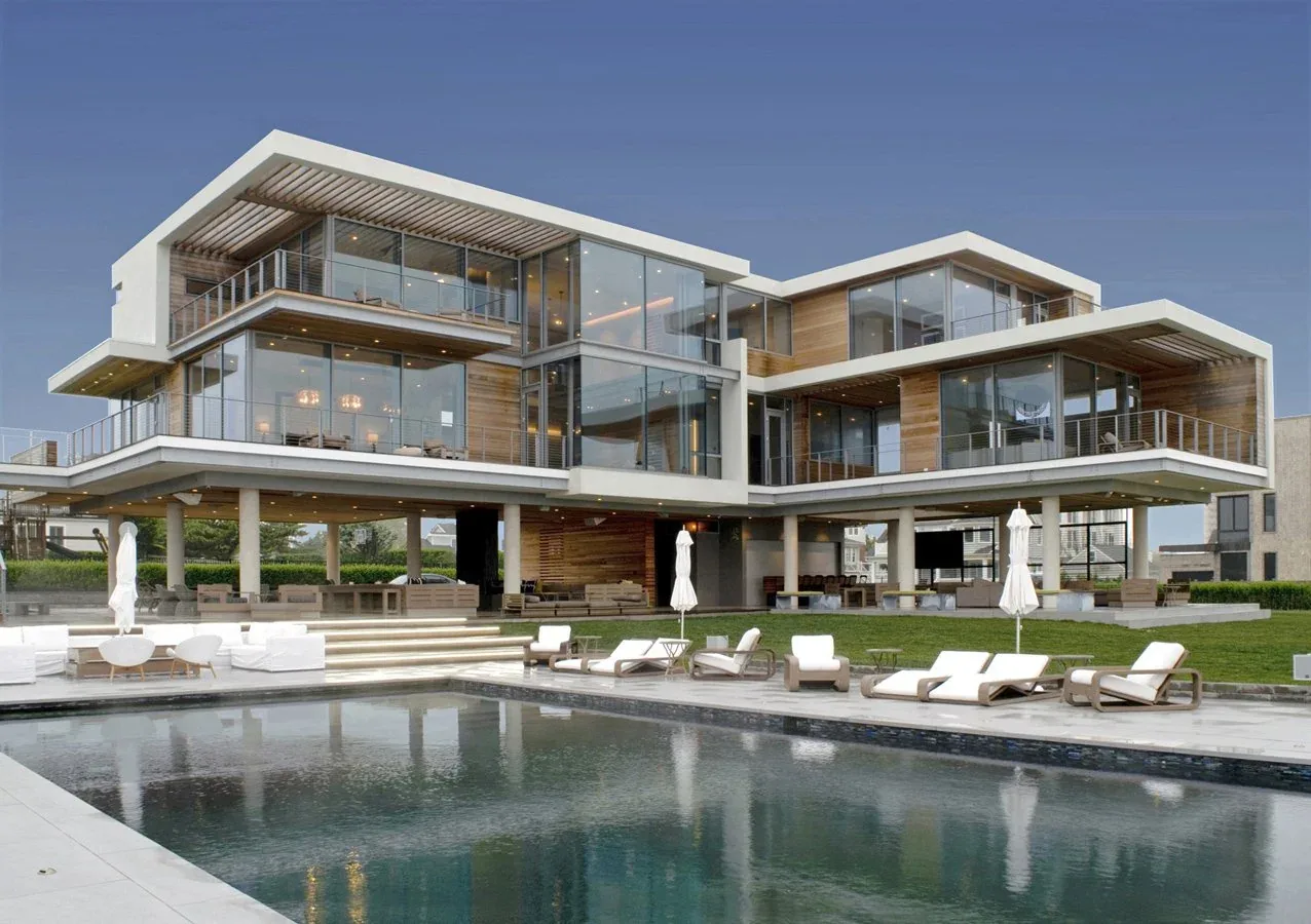 Exterior view of a modern multi-level house with extensive glass walls and a pool in front.