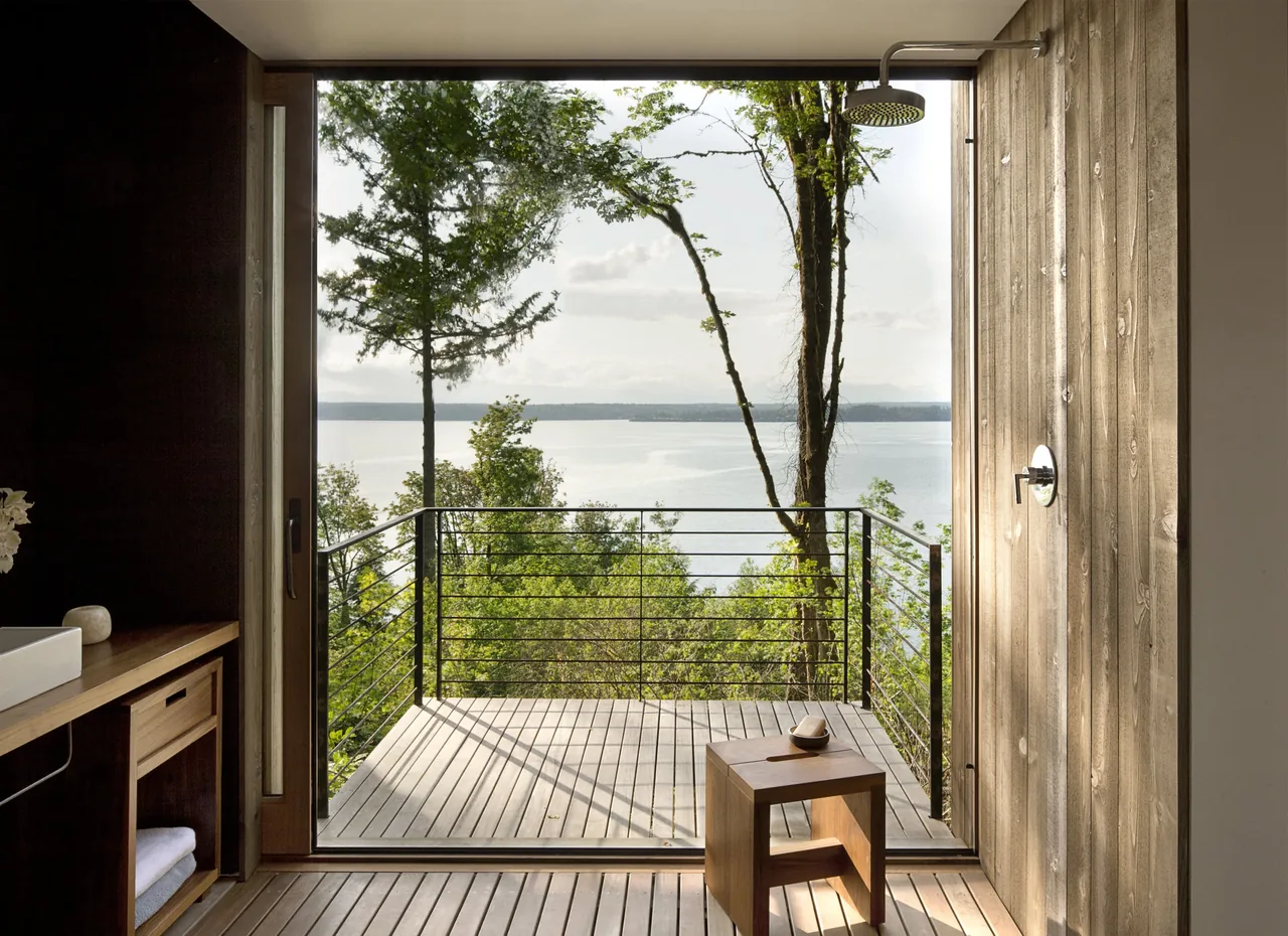 Outdoor shower with vertical wood siding and a lake view beyond a metal railing deck.