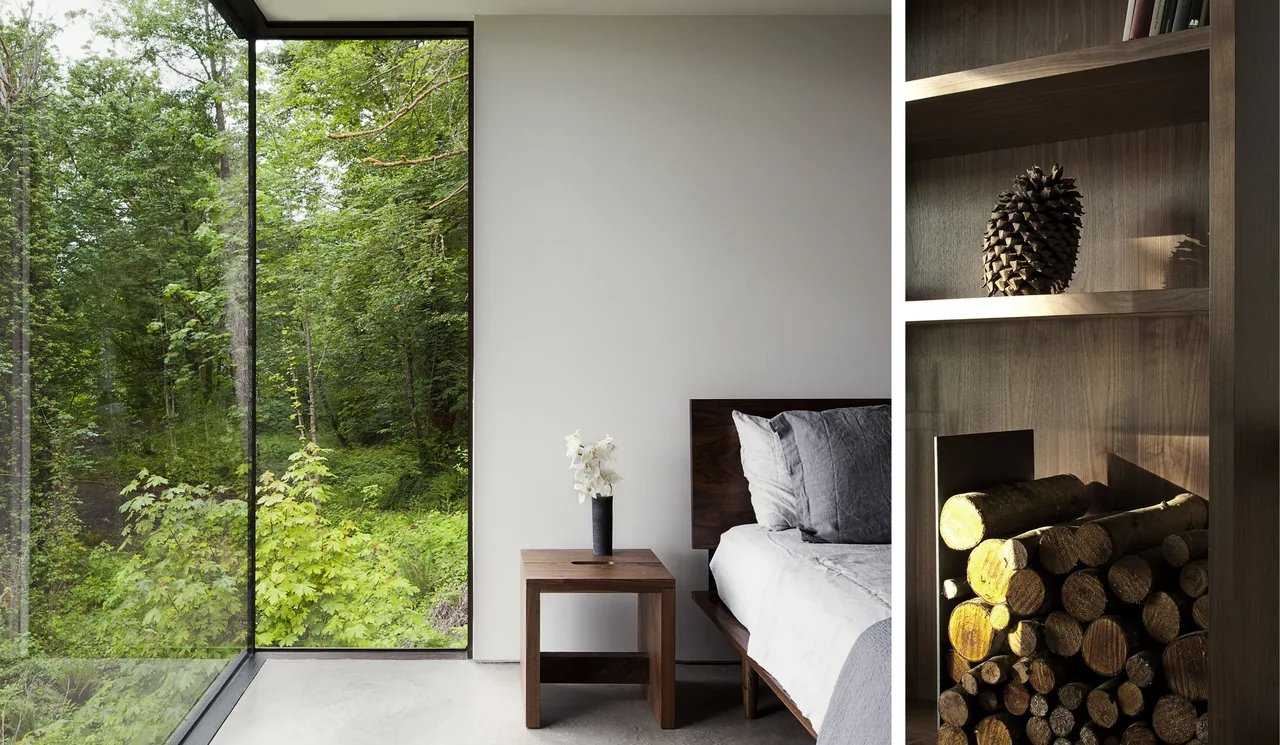 A bedroom corner featuring floor-to-ceiling glazing overlooking a forest and a wood nightstand beside the bed