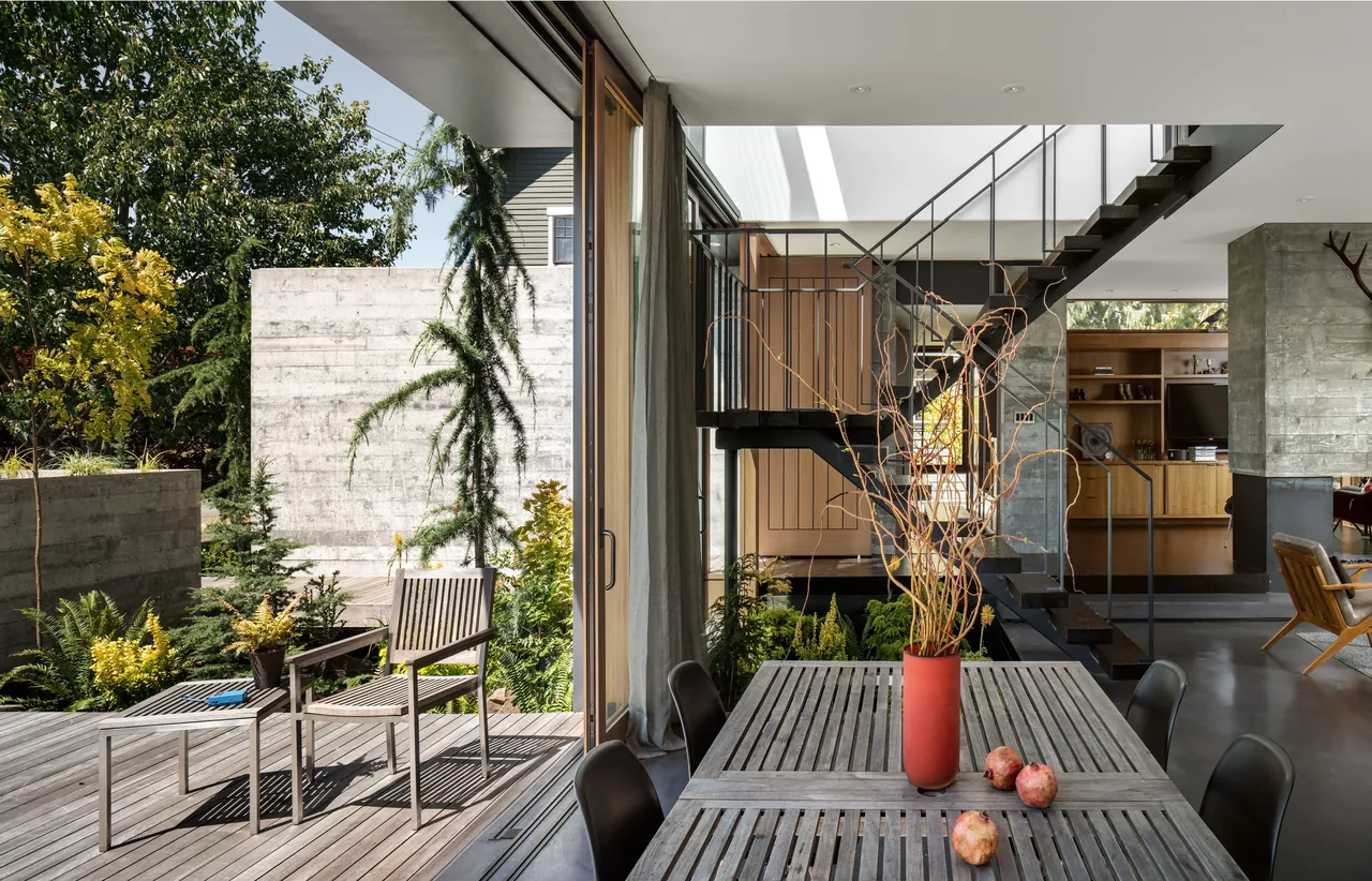 Magnolia residence with an open dining room connecting to an outdoor wooden deck, featuring a concrete fireplace and black steel staircase.