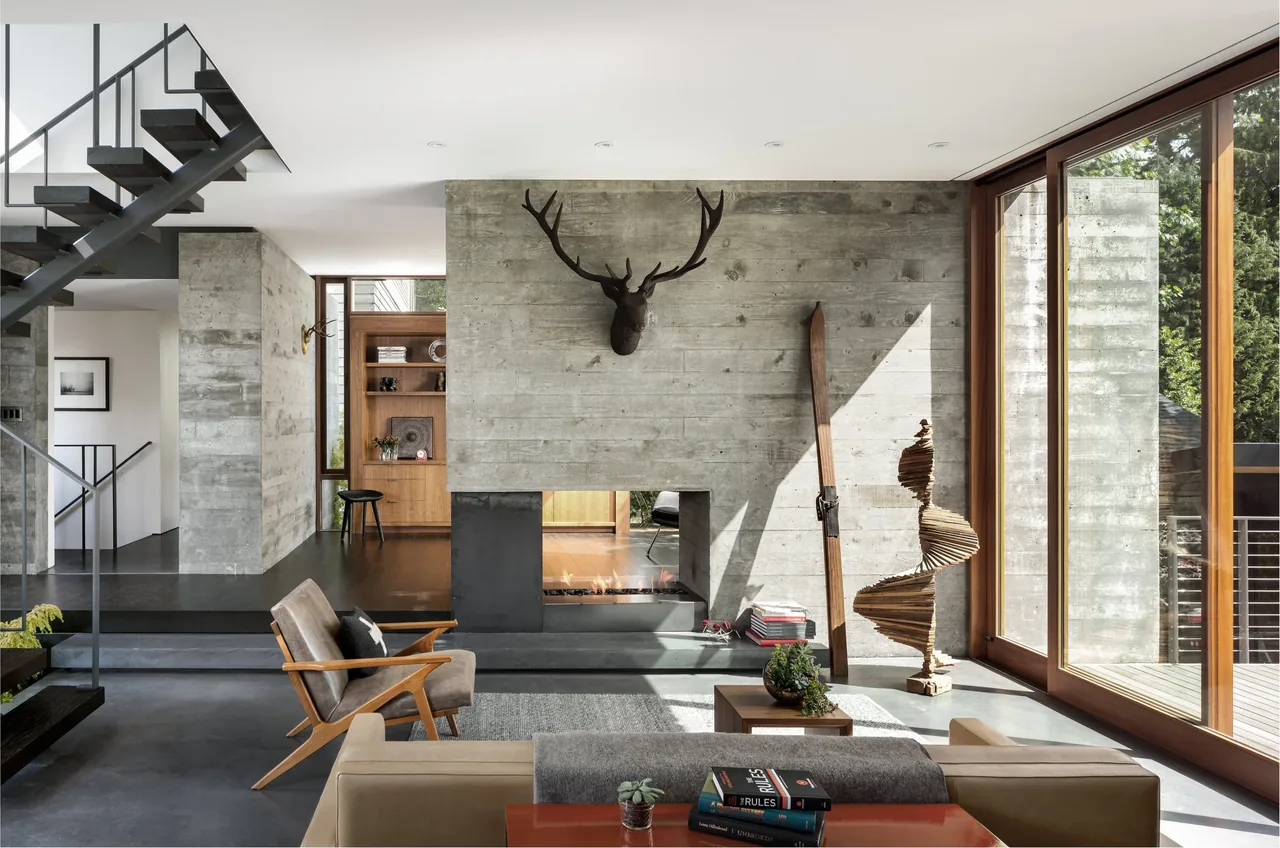 The living room features a concrete wall fireplace, a mounted deer head, and large wood frame glass doors leading to a deck.