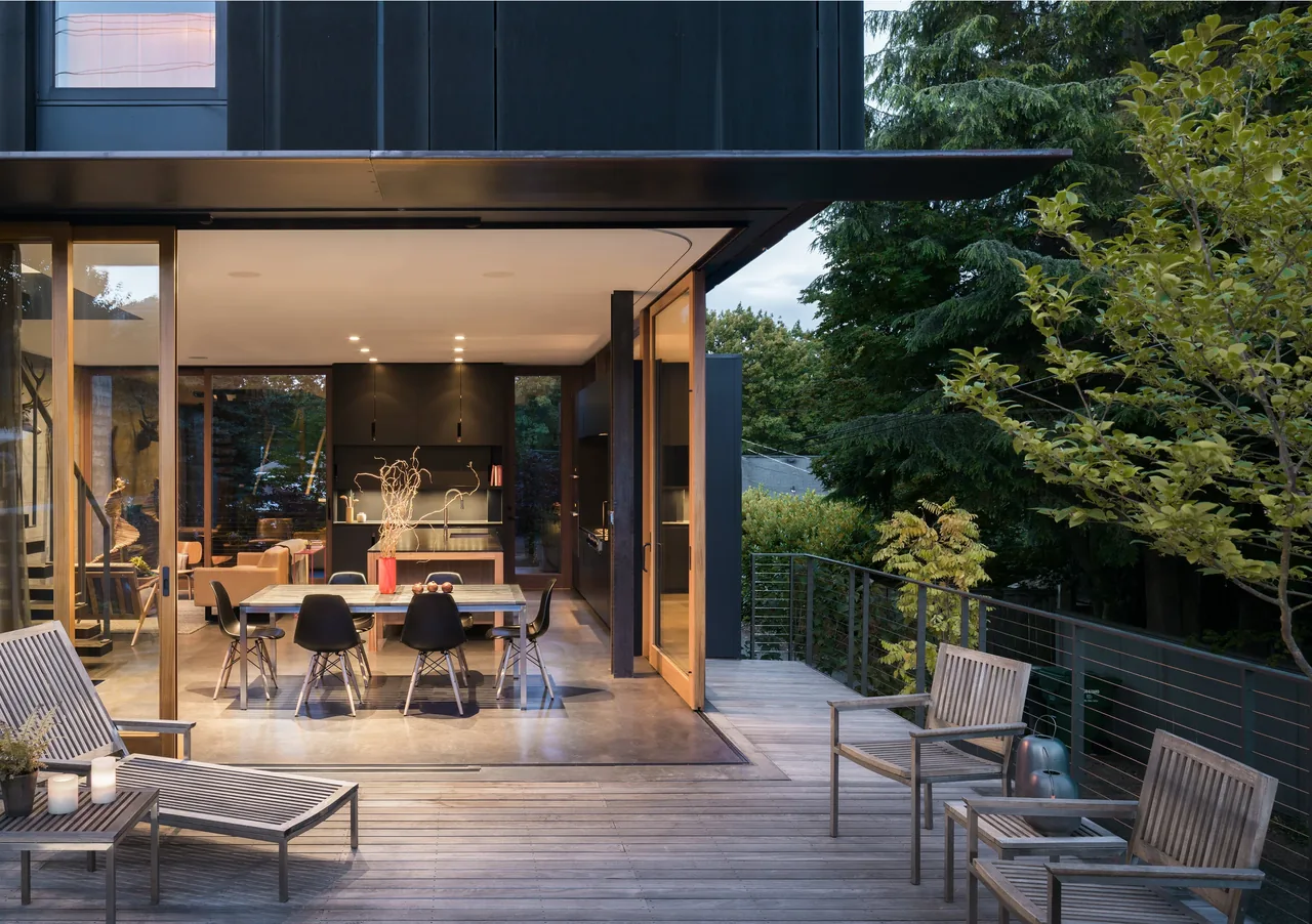 Magnolia Residence features a dining area opening to a wooden deck with seating, achieved through large sliding glass doors.