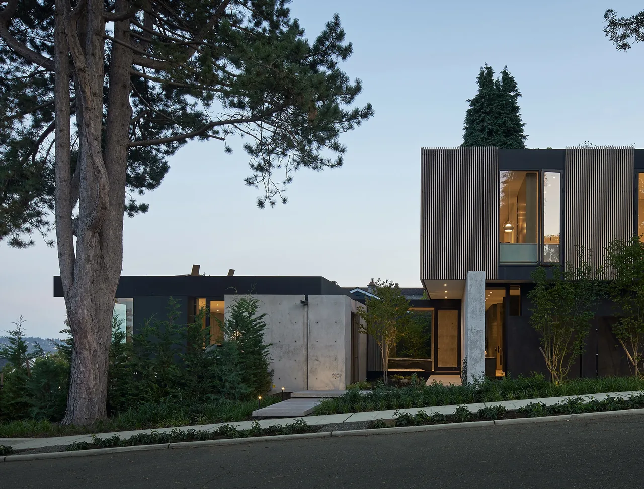 Exterior view of Magnolia residence with vertical wood siding, concrete walls, and landscaped greenery.
