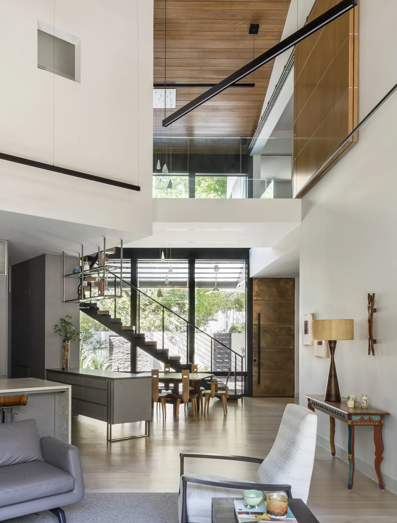Open-concept living and dining area with a metal staircase and expansive glass walls connecting indoor and outdoor spaces.