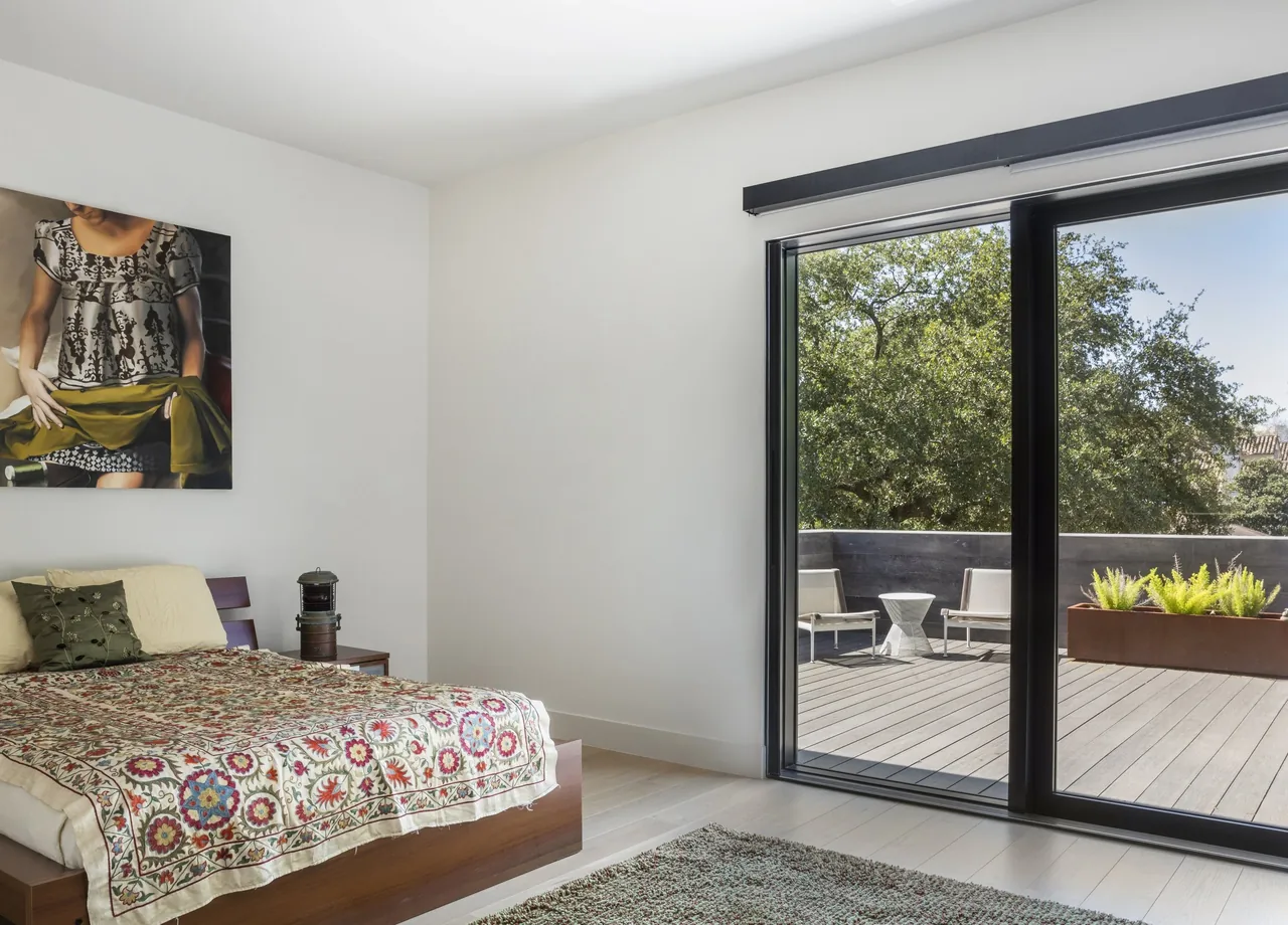 Bedroom with wooden bed frame and sliding glass door overlooks a deck with seating and greenery at Shetland Lane House.