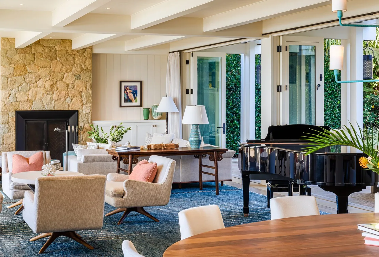 Living room features a stone fireplace, beige furniture, and a black grand piano near large folding glass doors.