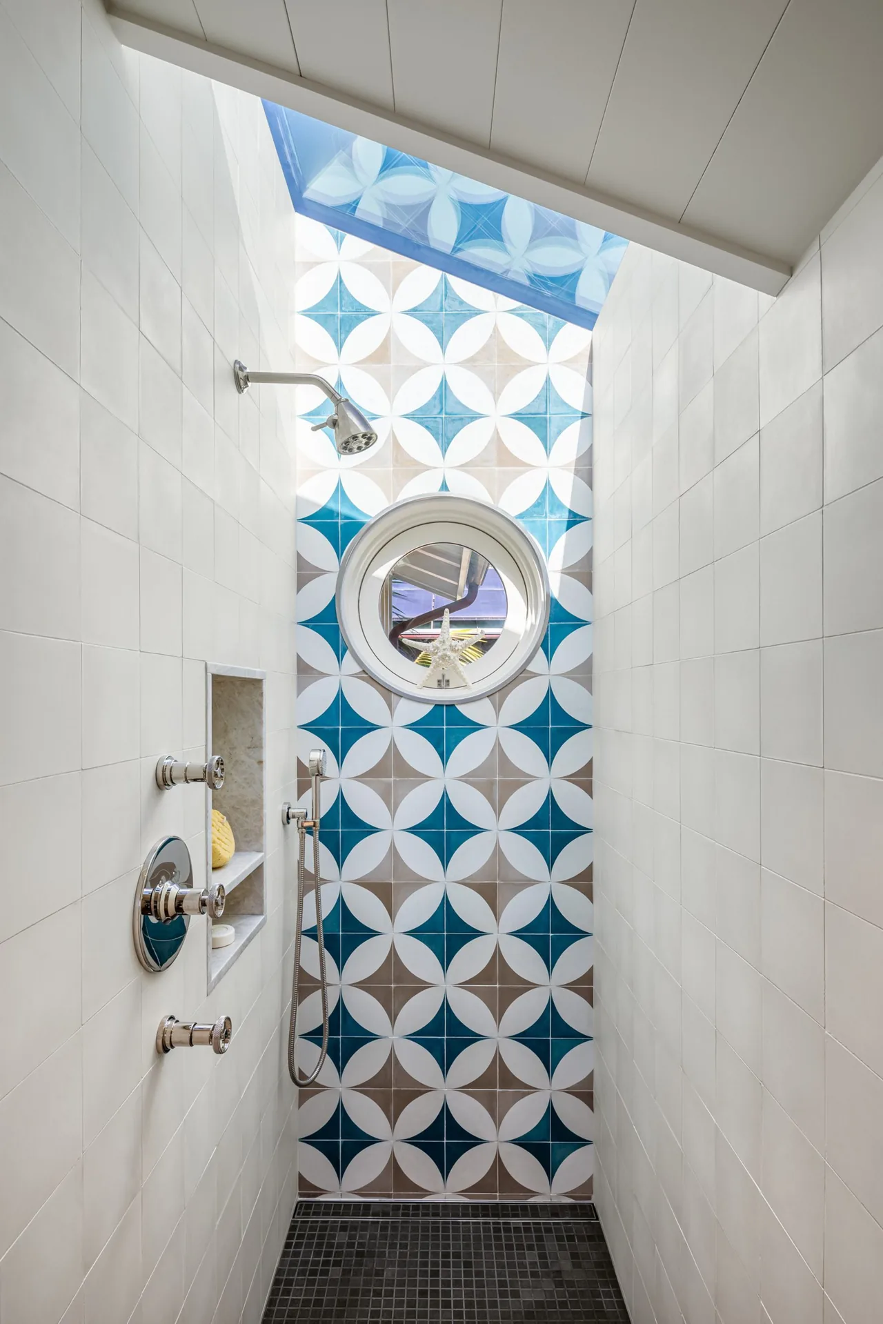 Bathroom shower with decorative blue and white patterned tiles and a round window above.