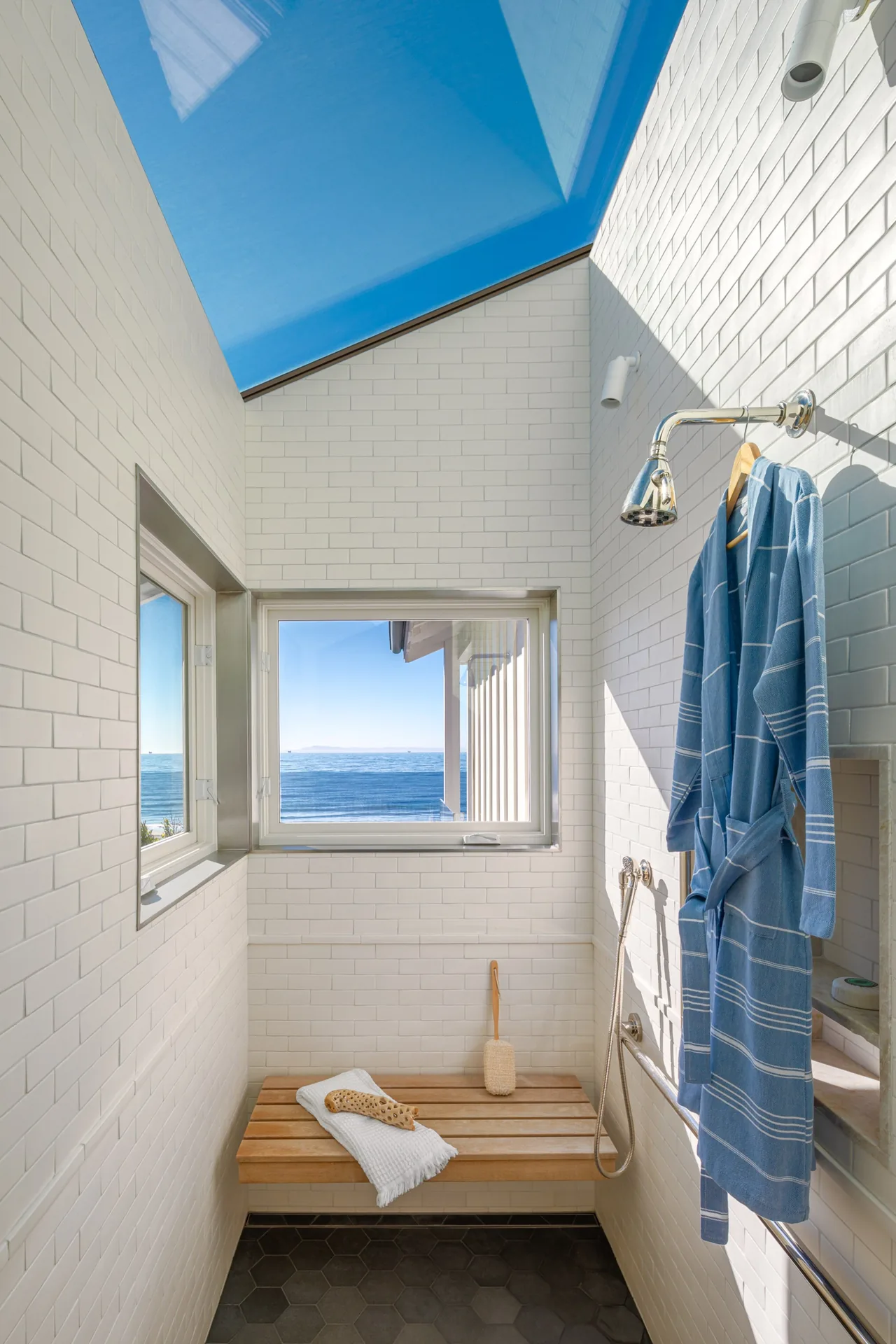 Shower with subway tile walls, wooden bench, and window overlooking ocean in the Padaro Beach Home project.