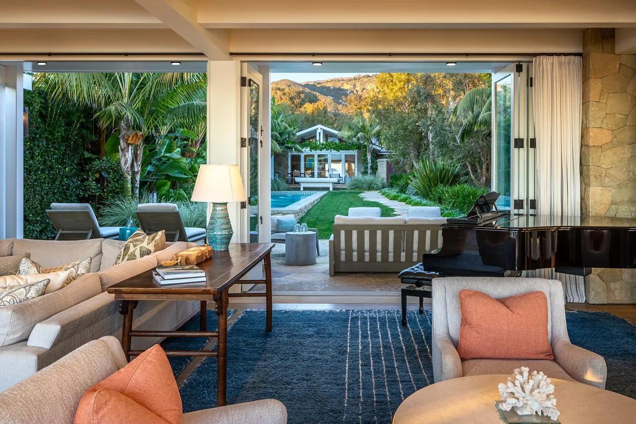 Living room featuring folding glass doors opening to a green backyard with pool and seating area under a mountain backdrop.