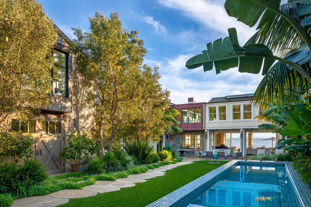Padaro Beach Home features a backyard with a pool, green lawn, and ocean view framed by a modern home's architecture.