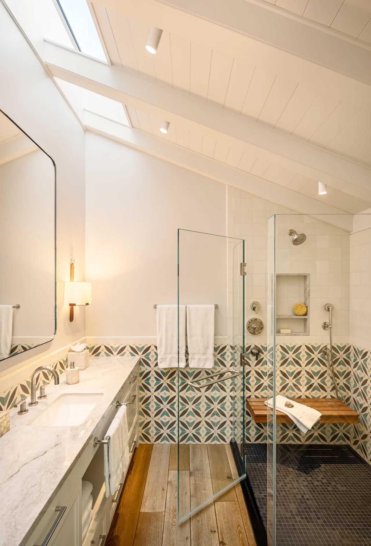 Bathroom featuring a glass-enclosed shower with decorative tile wainscoting and wood plank flooring under a vaulted ceiling with skylights.