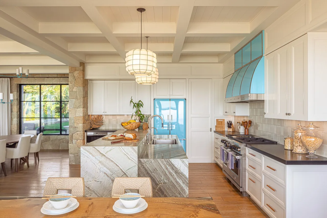 Kitchen features a marble island, blue range hood, stainless appliances, and white cabinetry in a home designed by Neumann Mendro Andrulaitis Architects.