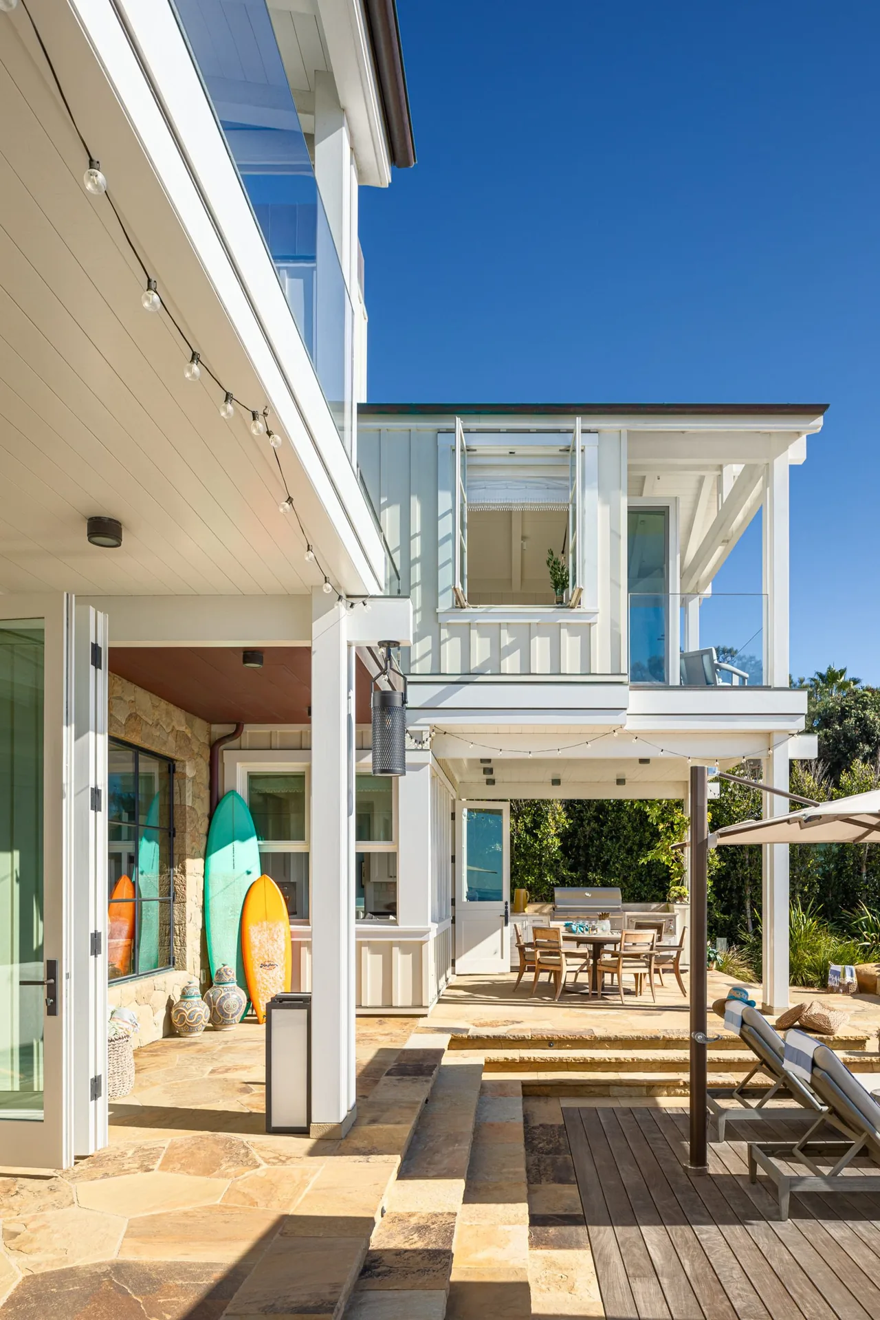 Exterior patio and balcony of Padaro Beach Home shows an outdoor dining area, string lights, and lounge seating.