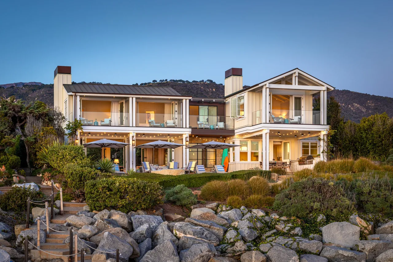 Padaro Beach Home features balconies, outdoor seating areas, and a view over rocky landscaping toward hills.