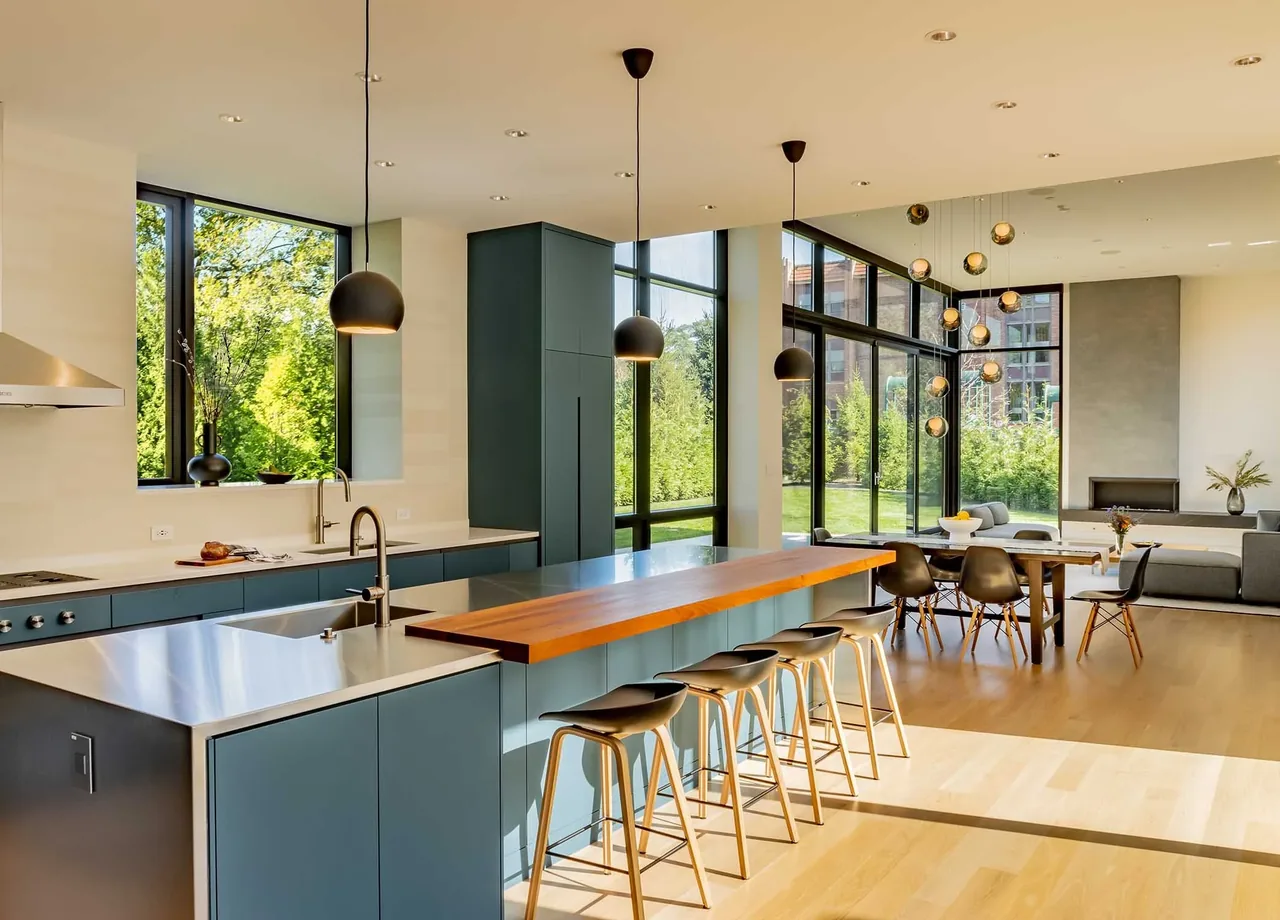 Open kitchen and living space with black-framed windows, a wooden floor, pendant lighting, and a dining area beside the fireplace.