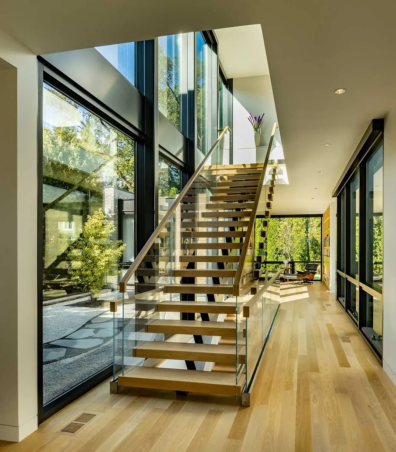 Floating wooden stairs with glass balustrade next to expansive black-framed glass walls.