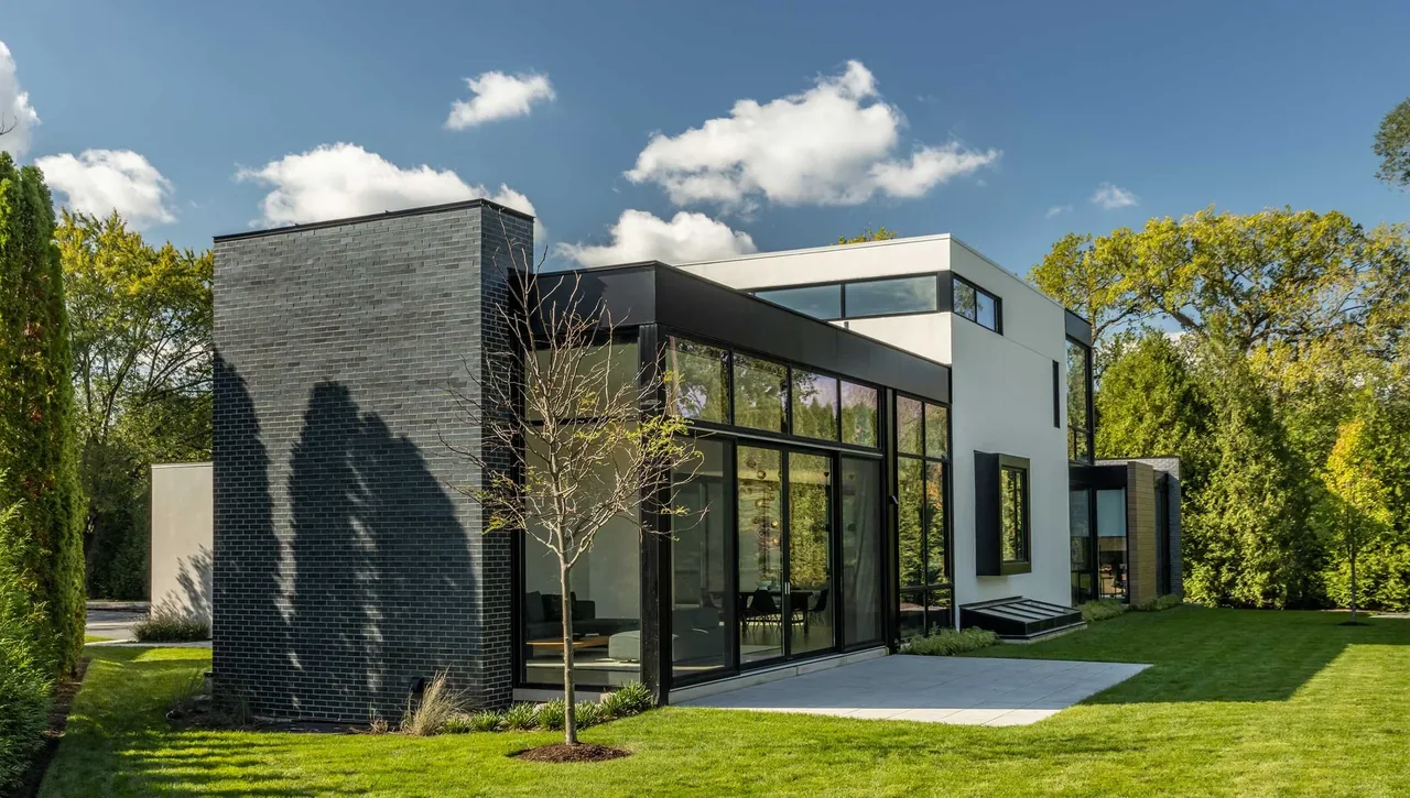 Modern house exterior featuring black brick, white stucco, large black-framed windows, and a landscaped lawn in Wilmette.