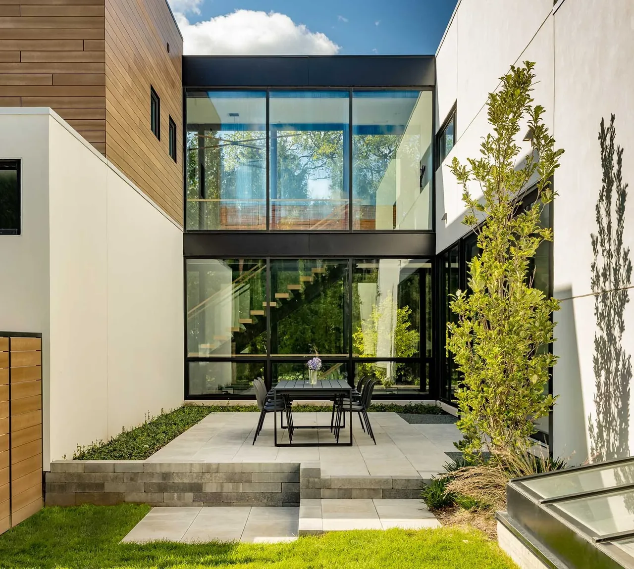 Courtyard patio area featuring a black metal framed glass wall with interior floating stairs and adjacent landscaping.