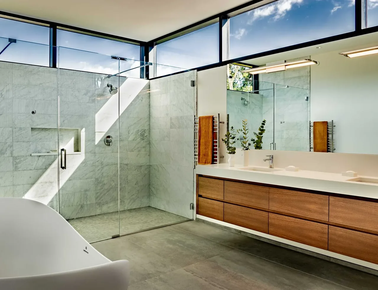 This Wilmette bathroom features a glass shower with marble tile walls and a wood vanity beneath clerestory windows.