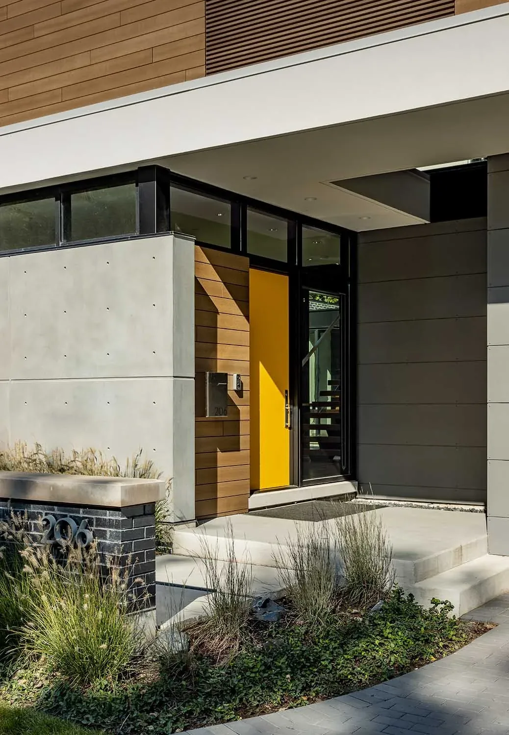 Modern home entry featuring a yellow front door, concrete planter with house number, and mixed material facade.