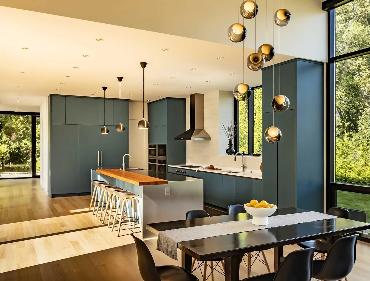 Kitchen and dining space featuring blue cabinets, a wood-topped island, pendant lights, and large black-framed windows with garden views.