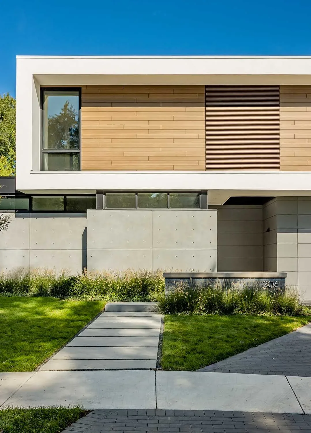 Front exterior of a modern house featuring wood siding and smooth concrete walls with a paved walkway.