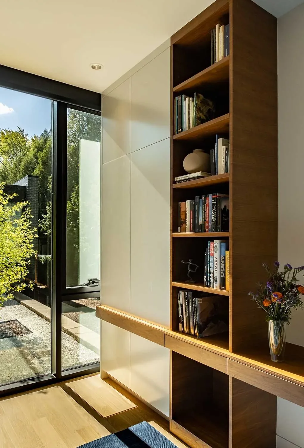 Corner of a room features built-in wood bookshelves and a large floor-to-ceiling window with black frames.