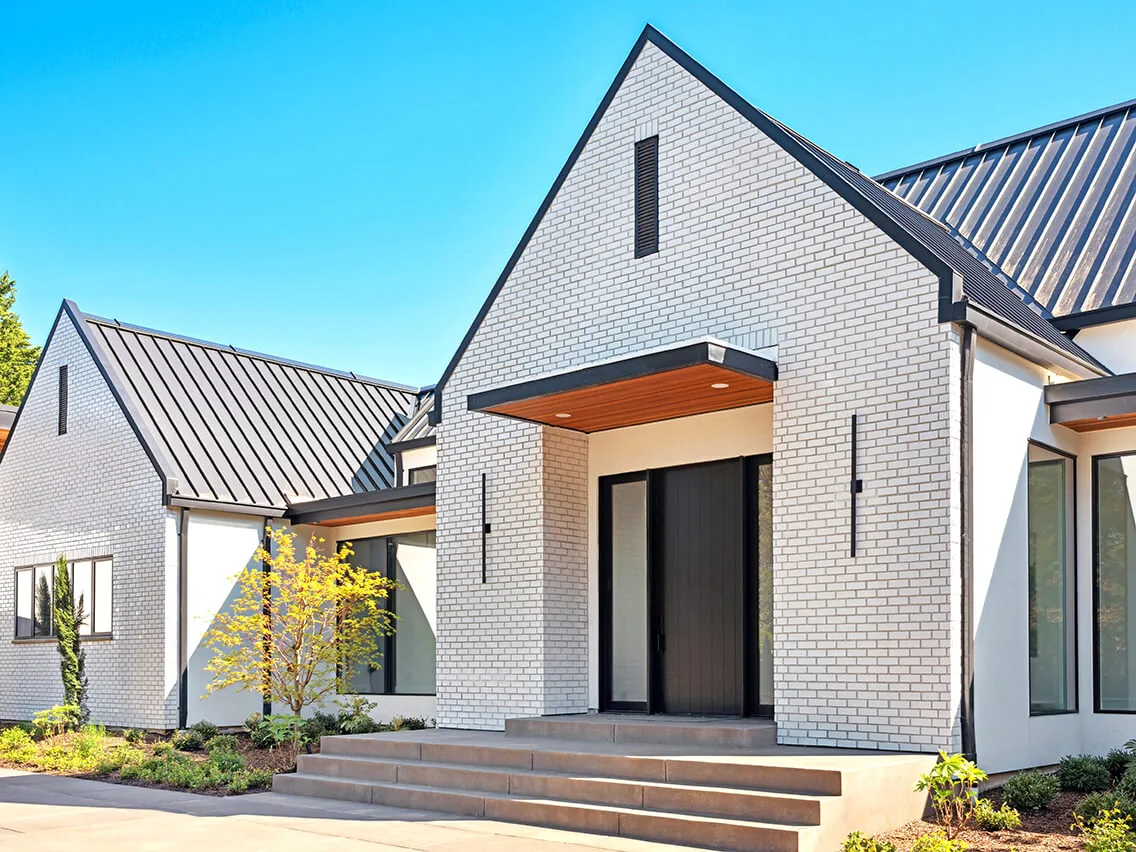 Exterior front of BURTON NEW CUSTOM BUILD showing white brick facade, black metal standing seam roof, and covered entry with black door.