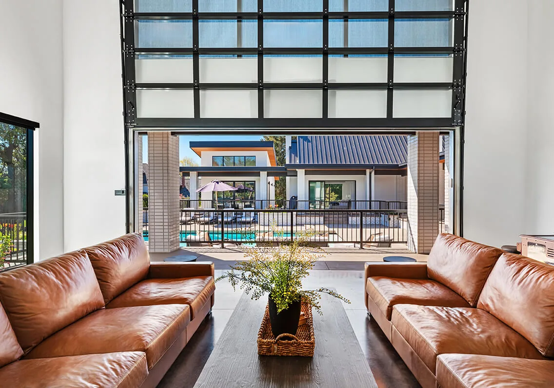 The living room features brown leather sofas and a large glass door opening to a patio with pool views in the BURTON NEW CUSTOM BUILD project.