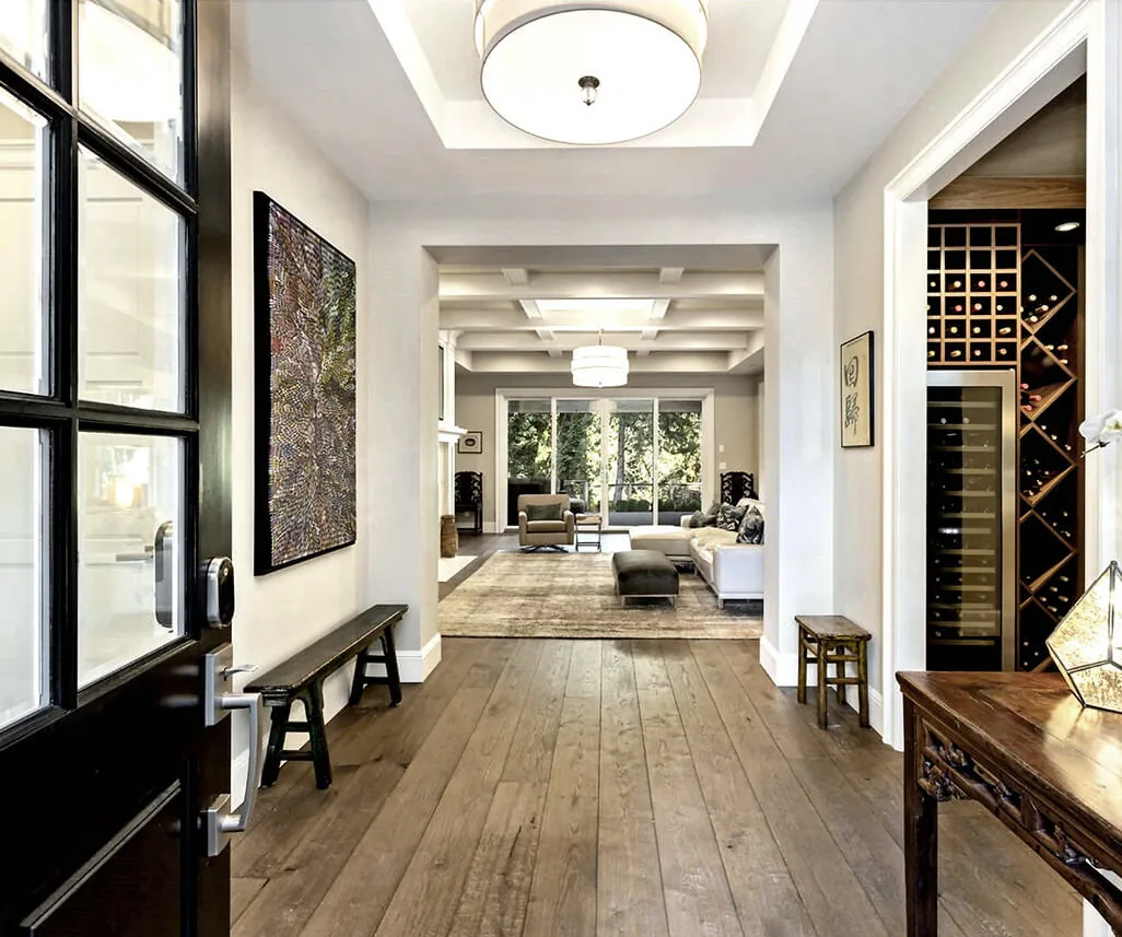 Entry hallway with wood flooring leads to a living room featuring a coffered ceiling and large sliding glass door.