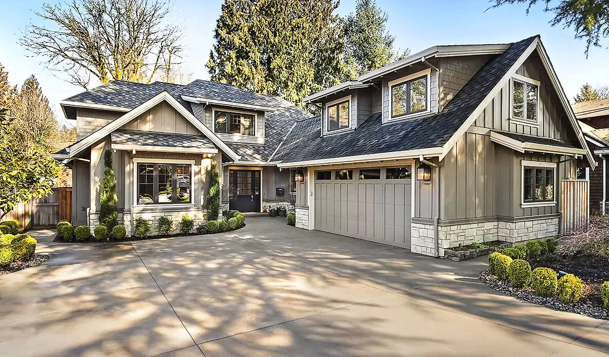 Front view of a two-story house with gray siding, stone accents, and a driveway leading to a garage.