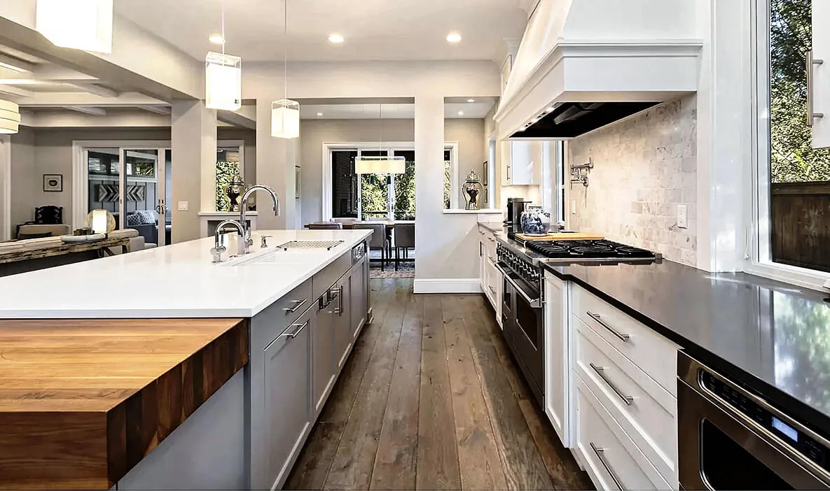 Modern kitchen with a center island, gas range, and large windows overlooking greenery.