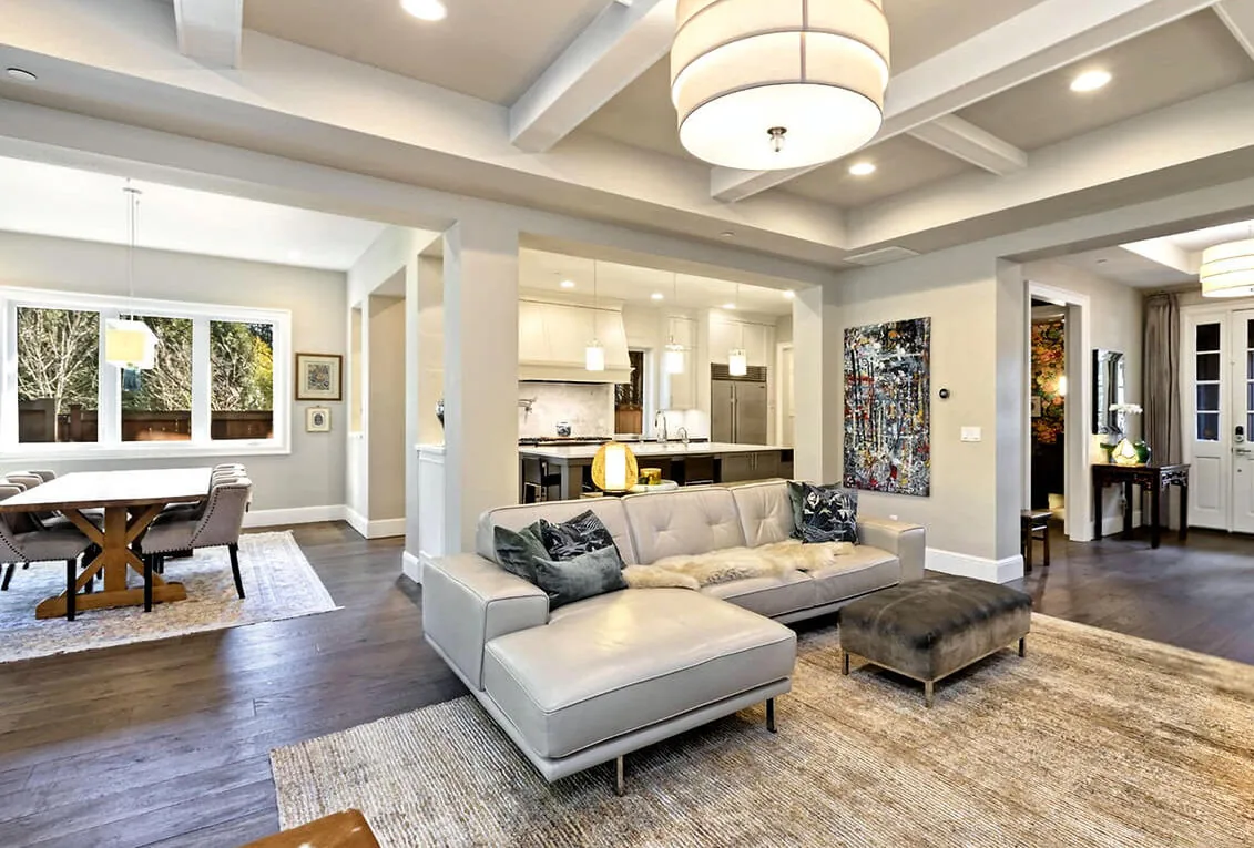 Open living room with a beige sectional sofa, wood floor, and exposed beam ceiling connects to kitchen and dining space in G STREET CUSTOM project.
