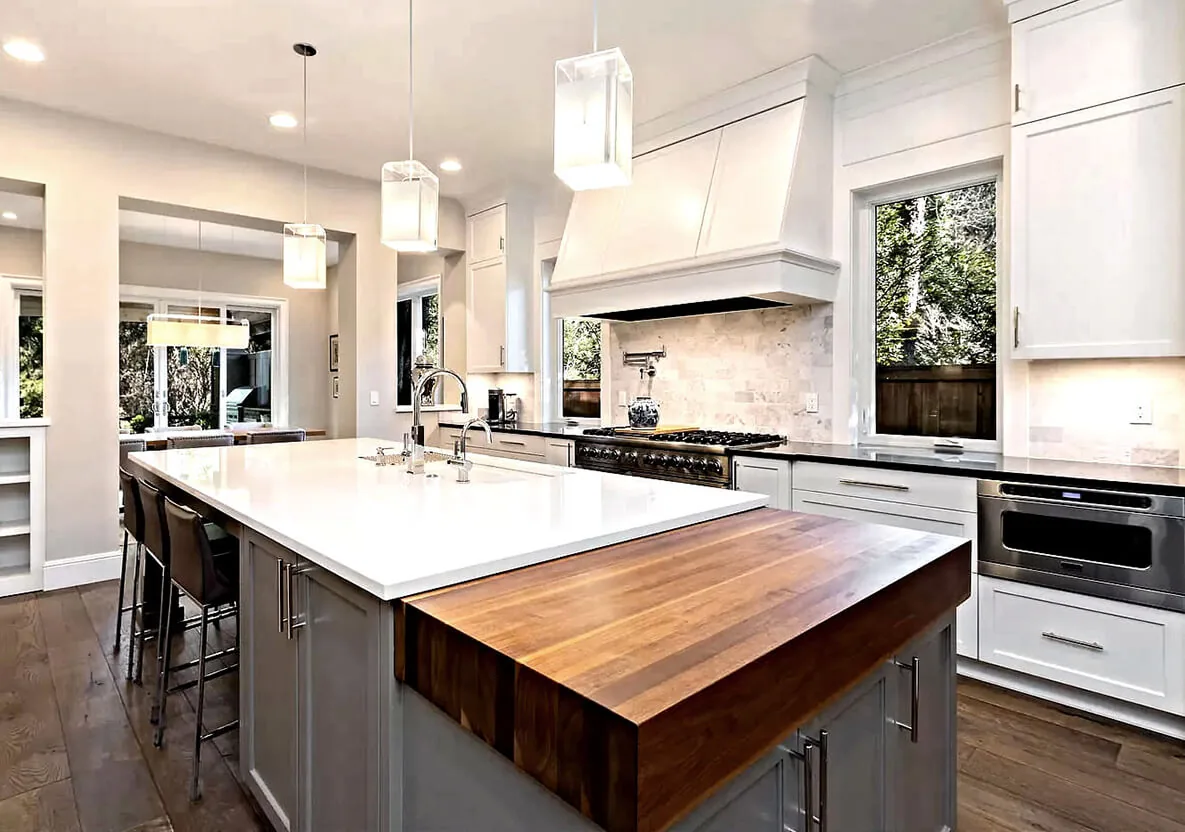 G STREET CUSTOM kitchen with a large island combining white quartz and a wood butcher block extension, showcasing pendant lighting.