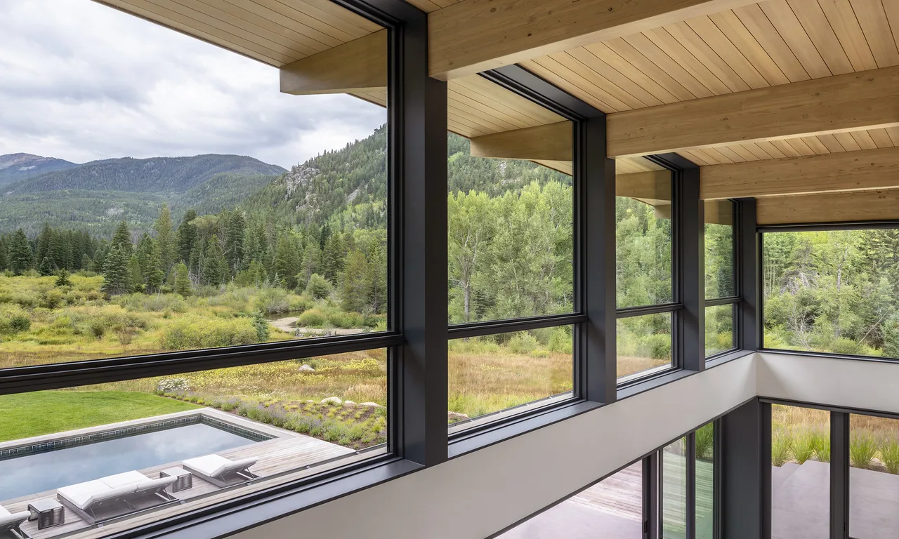 Room with floor-to-ceiling windows framing poolside deck and mountain views at Aspen Valley Home.