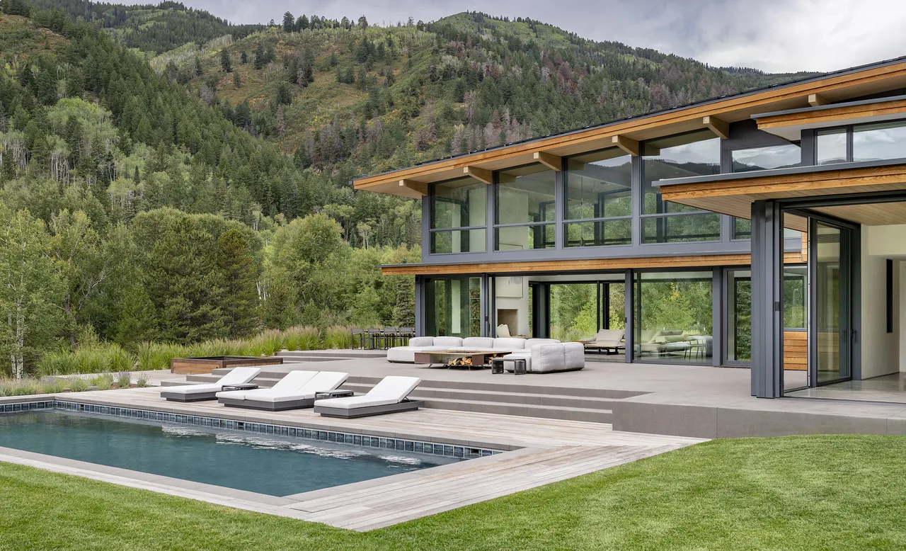 Aspen Valley Home features floor-to-ceiling glazing and a concrete pool deck with wood siding accent roof overhangs.