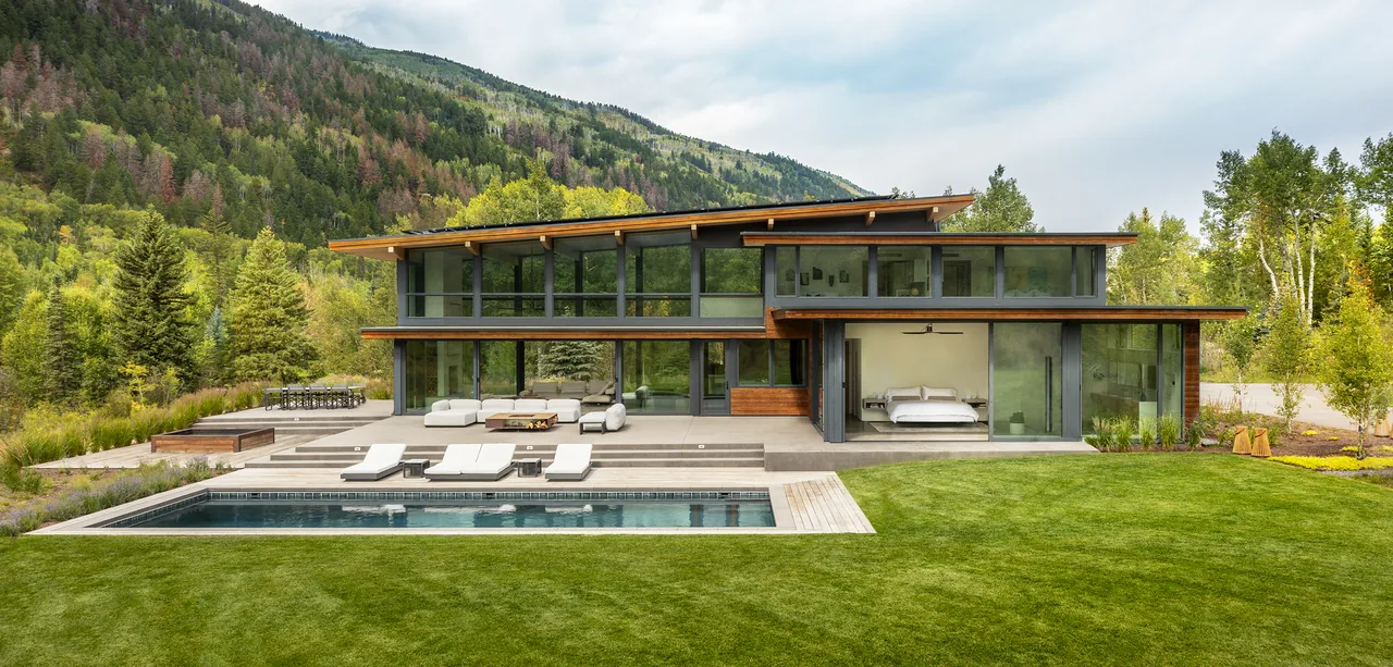 Aspen Valley Home in Aspen, Colorado features floor-to-ceiling glazing, wood siding, and a swimming pool patio against a mountainous backdrop.