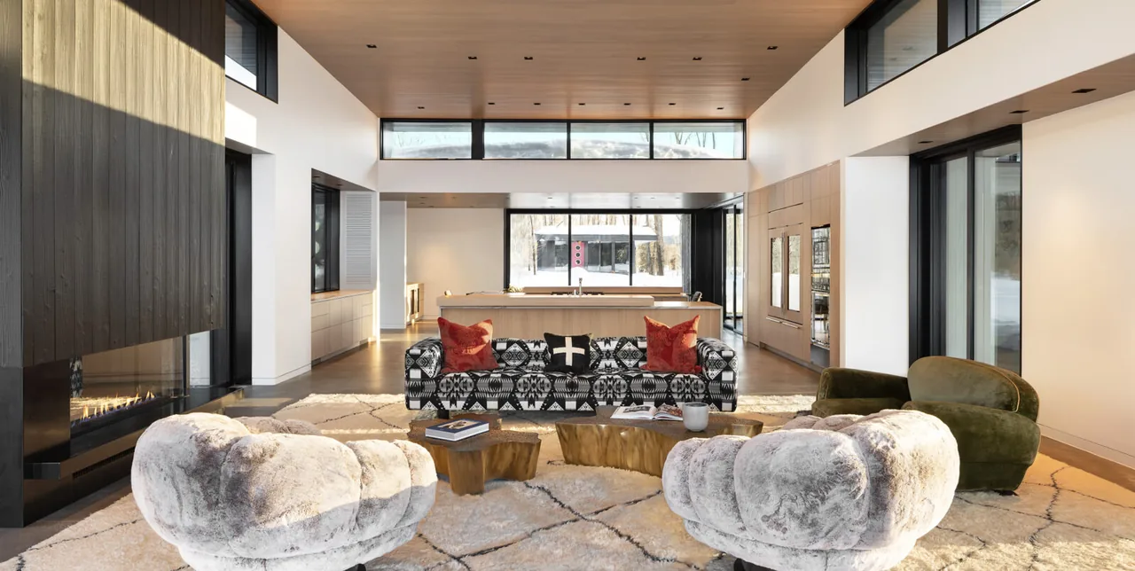 Open living room with patterned sofa, plush chairs, and a linear fireplace under high clerestory windows providing natural light.