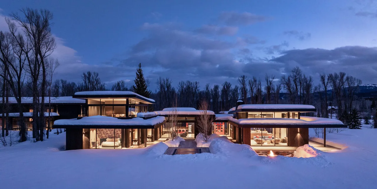 Thunder Road house in Jackson Hole features modern architecture with flat roofs and extensive glazing amid a snowy landscape at twilight.