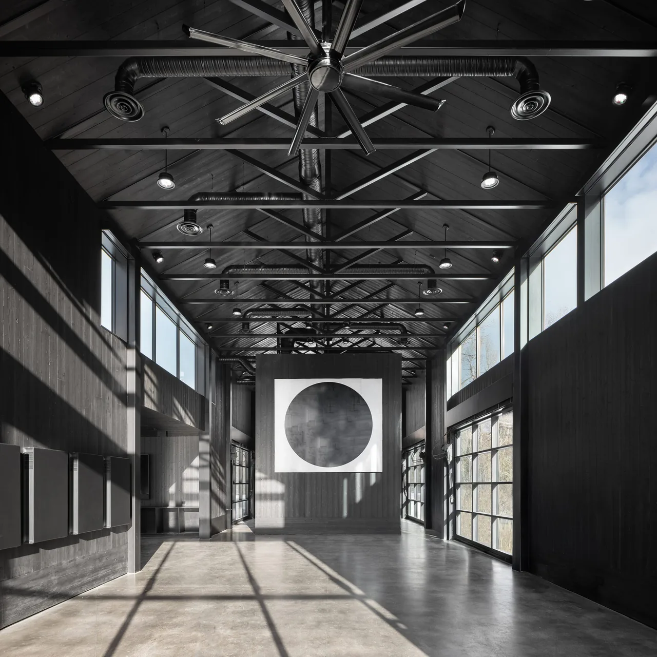 Spacious room featuring vaulted wood ceiling, large black-framed windows, and industrial ductwork with a modern art piece on the far wall.