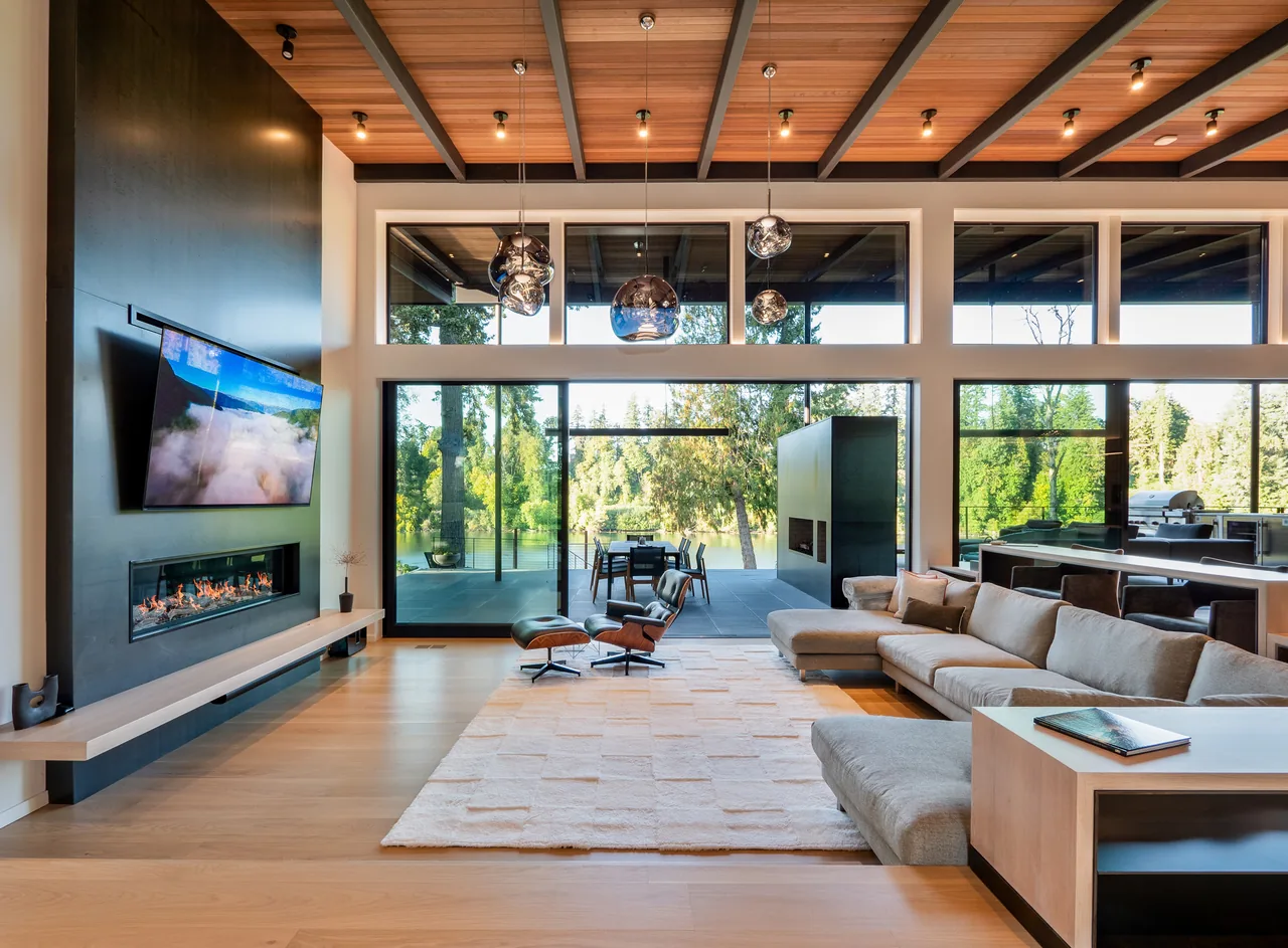 Living room features floor-to-ceiling windows and sliding glass doors that reveal a patio and waterfront view.