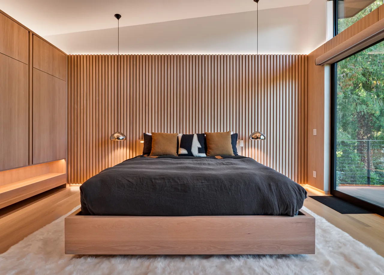 Bedroom featuring a wood slat wall, pendant lights, and large window with outdoor forest view.