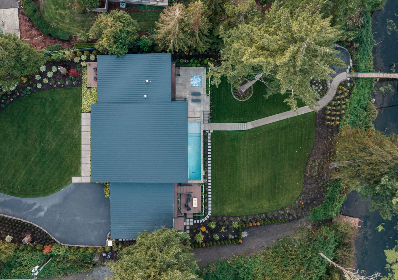 Montagne project by Paul McKean Architecture shows a home with a metal roof, a pool, and outdoor seating within a lush landscape.