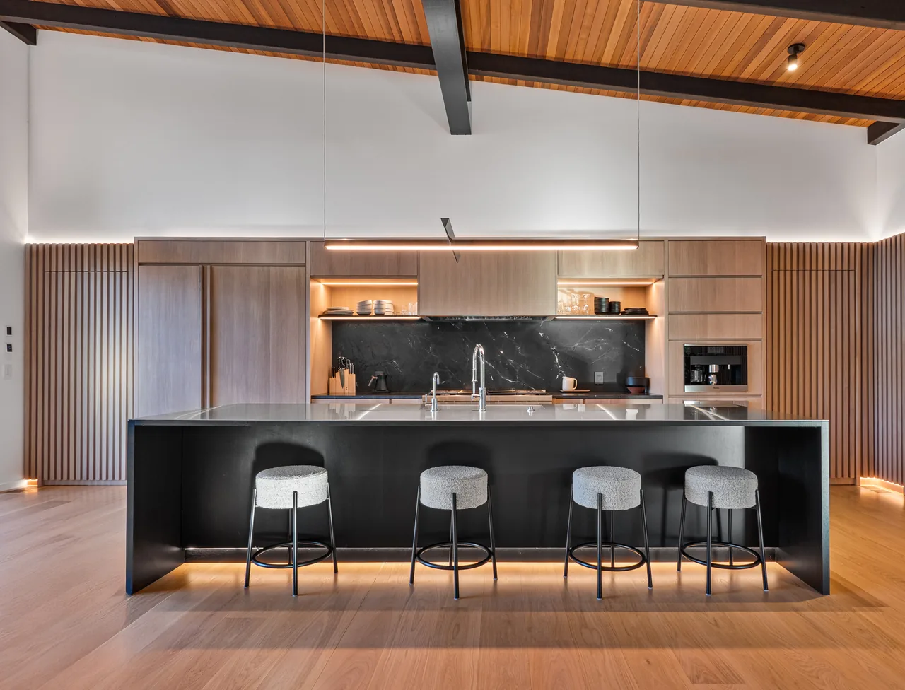 Kitchen with black island, wood cabinets, black marble backsplash, and wood-paneled vaulted ceiling with exposed beams.
