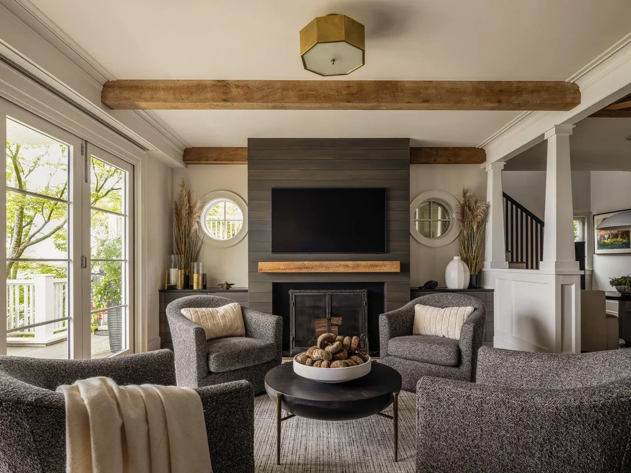 Living room with a fireplace, wall-mounted TV, exposed wood beams, and round windows flanking the fireplace.