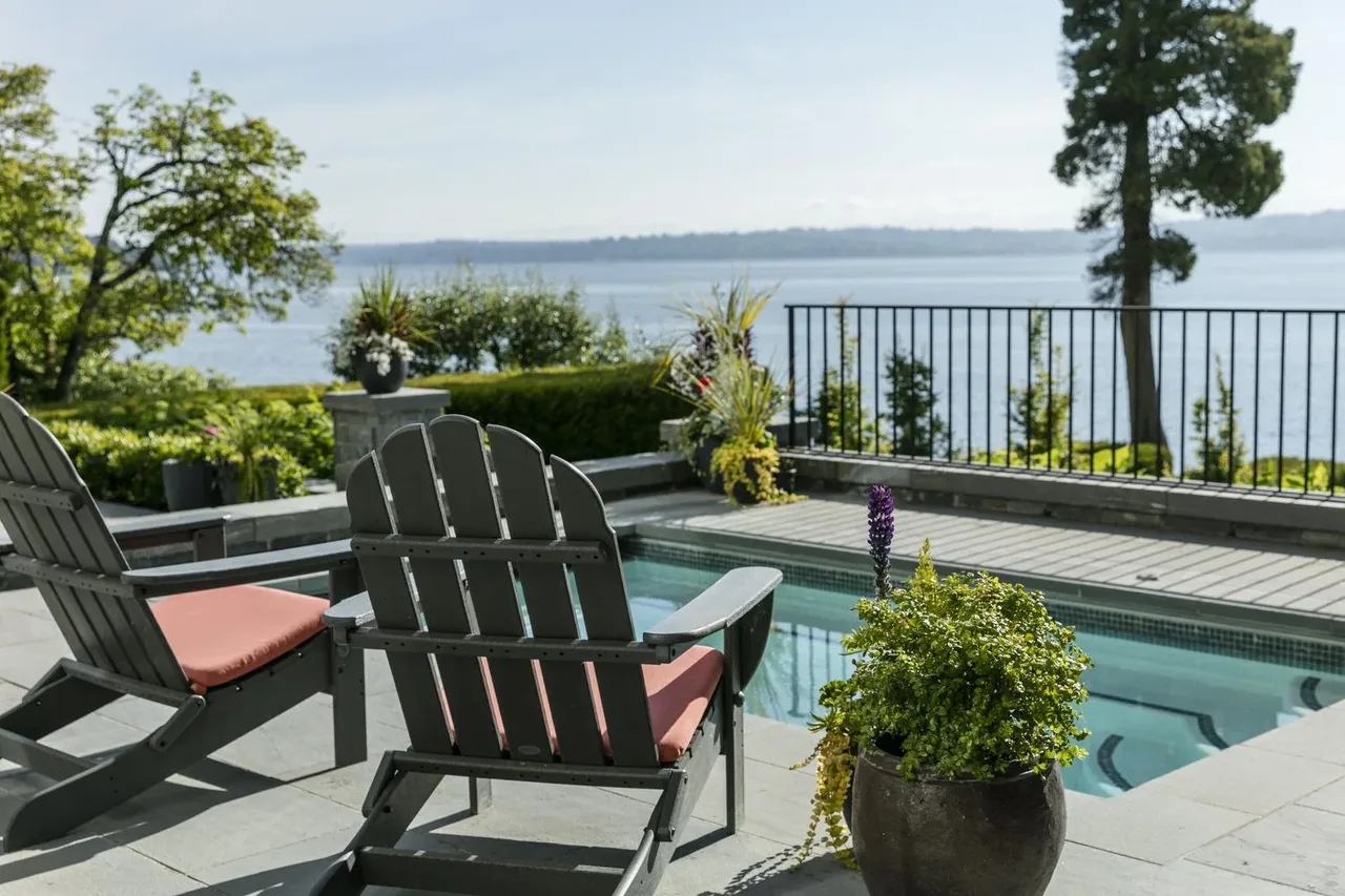 Outdoor seating area with Adirondack chairs by a swimming pool facing a lake view at Laurelhurst Contemporary.